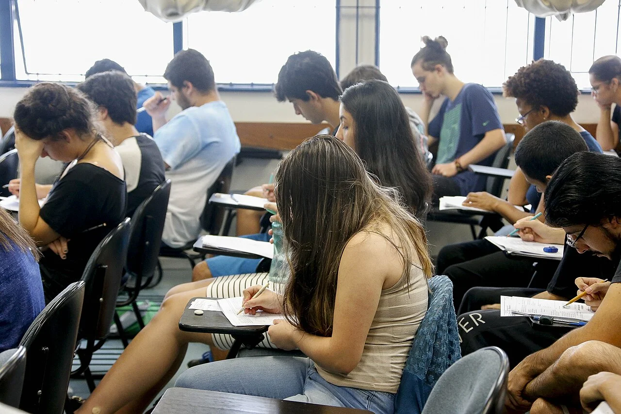 Candidatos realizando prova escrita de concurso público em sala de aula