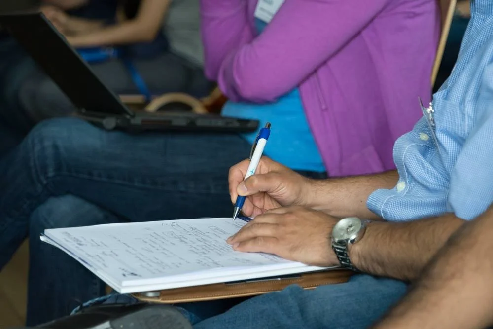 Estudante escrevendo anotações e sintetizando tópicos essenciais em caderno de estudos