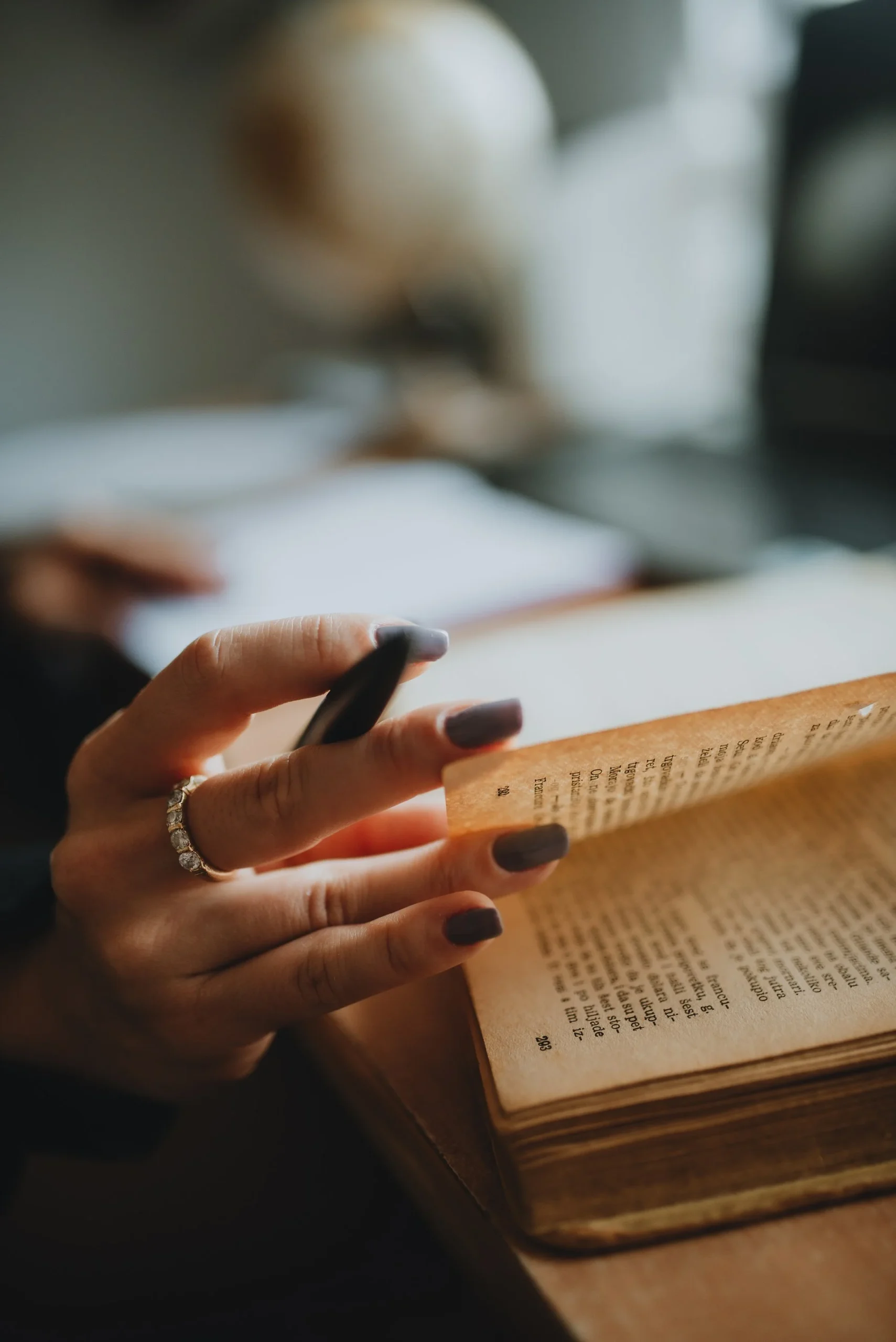 Pessoa estudando livro com caneta na mão em mesa organizada com foco pleno e iluminação acolhedora