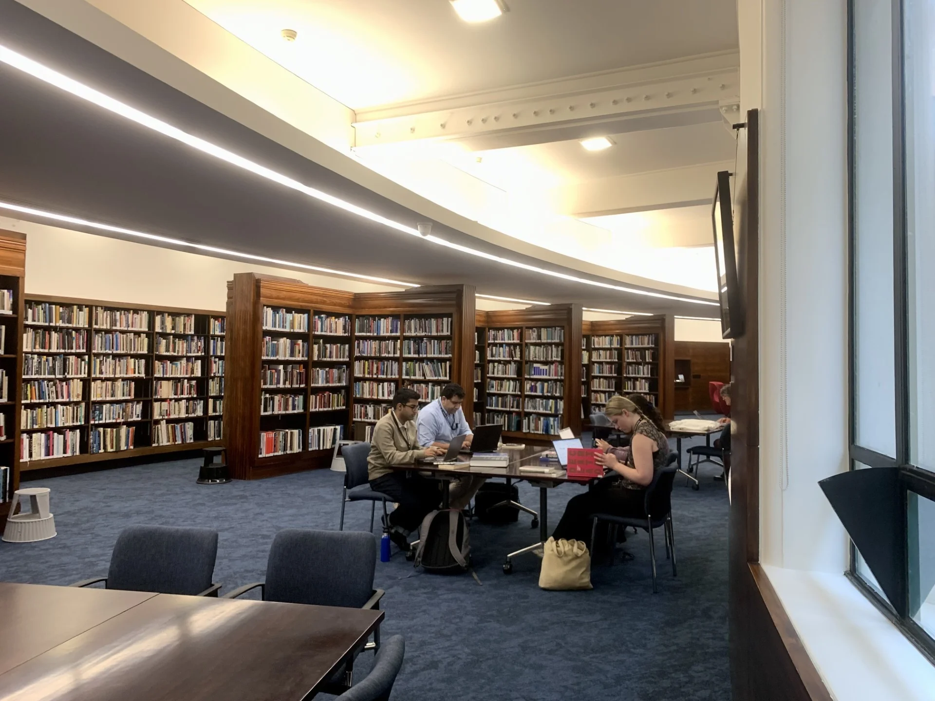 Estudantes realizando pesquisa e estudo ativo em biblioteca com computadores e materiais didáticos