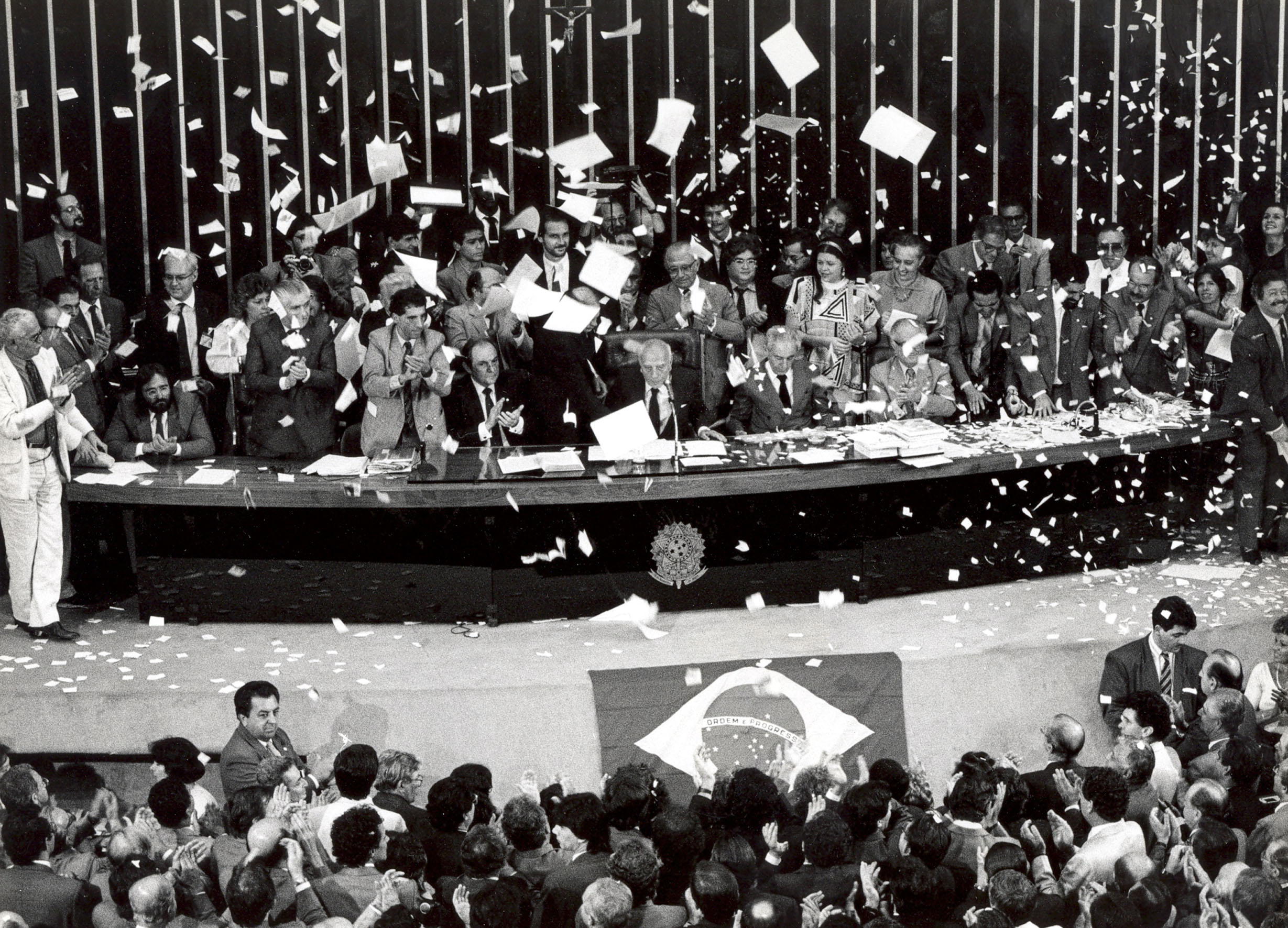 Fotografia histórica da promulgação da Constituição de 1988 por Ulysses Guimarães cercado por parlamentares e cidadãos