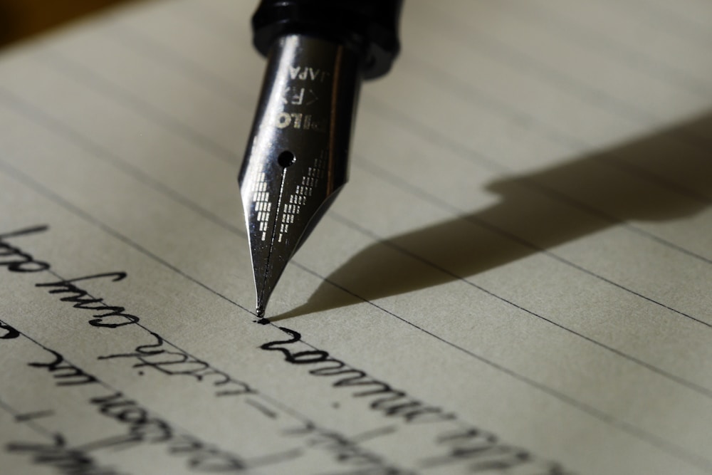 Pessoa concentrada escrevendo manuscrito em folha de papel com caneta preta sobre mesa de madeira